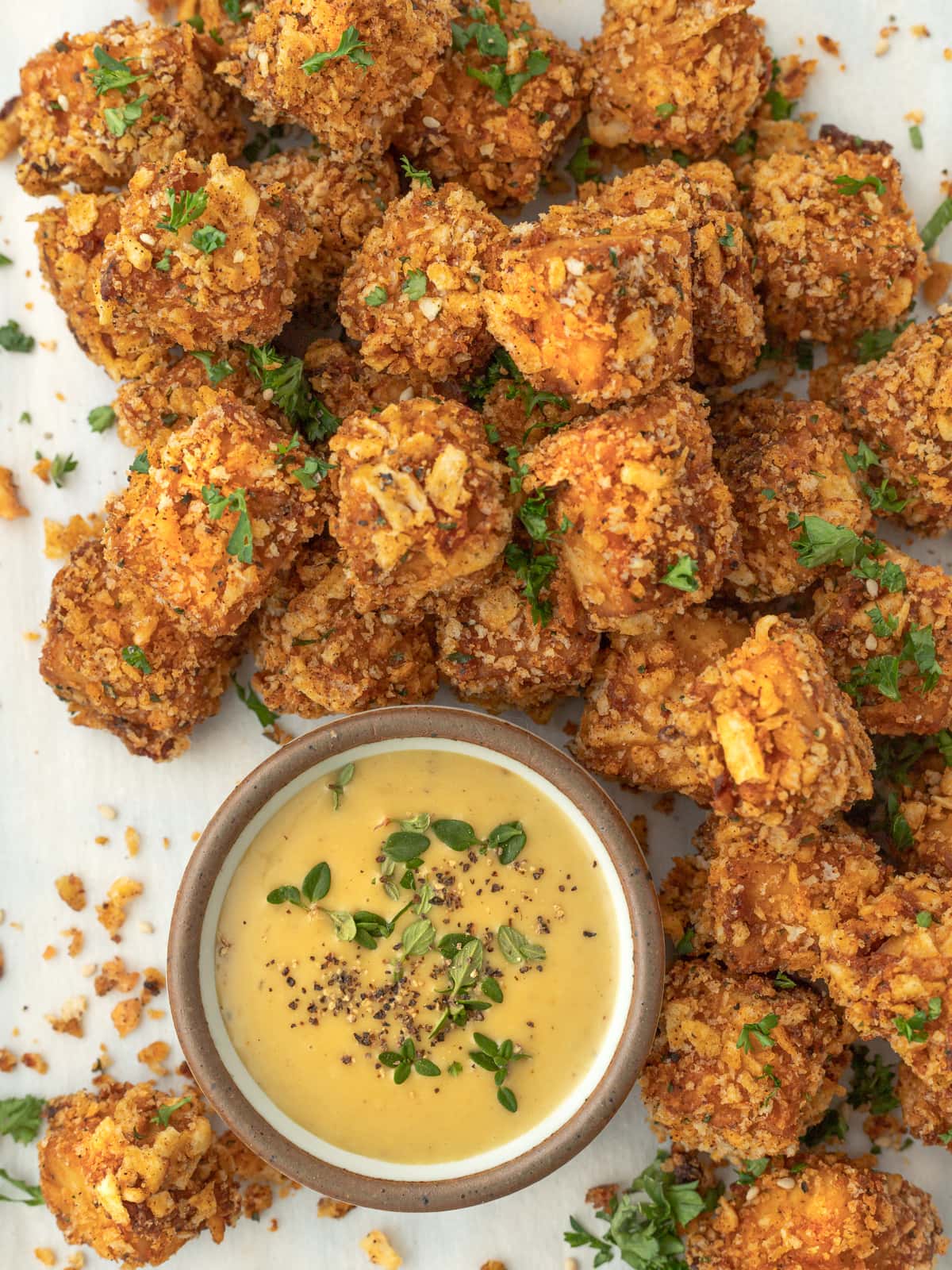 Pile of crunchy vegan chicken nuggets surrounding a dish of honey mustard sauce.