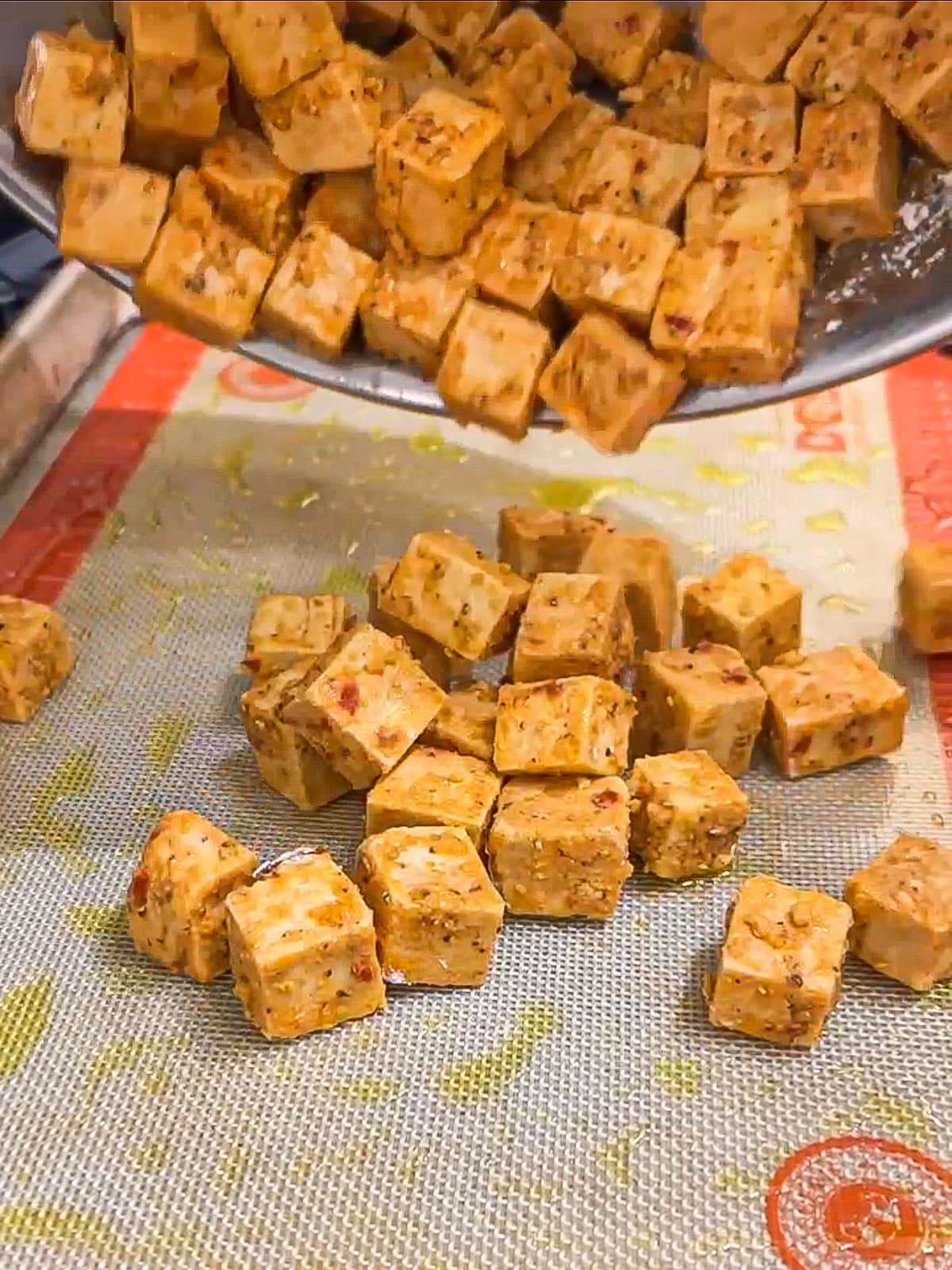 Seasoned tofu being poured on a baking sheet.