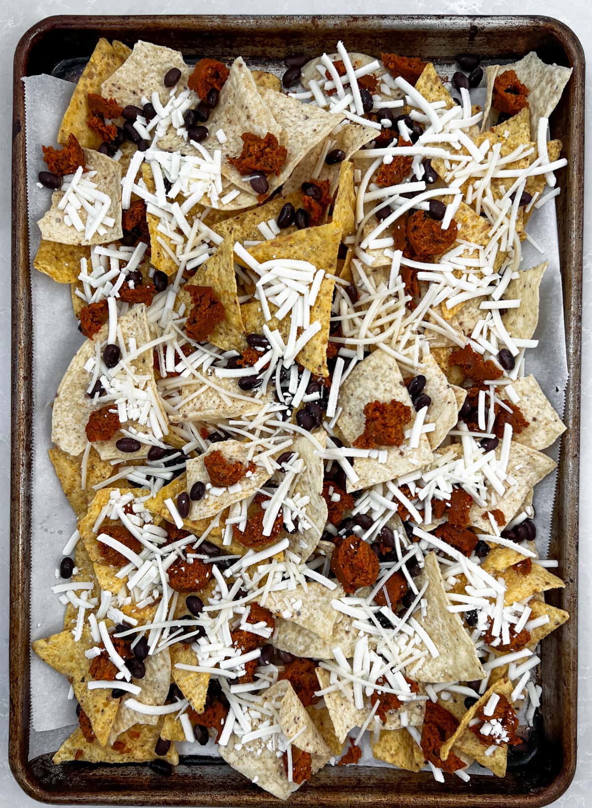 Layering vegan nacho chips on a sheet pan.