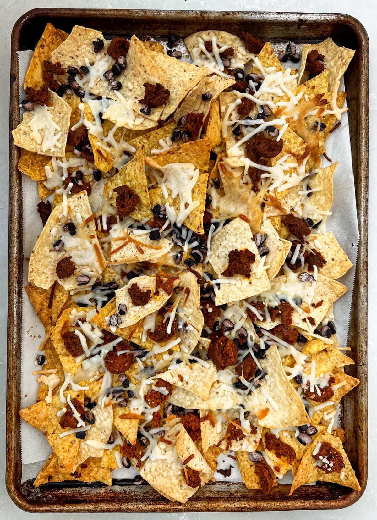 Sheet pan full of baked nachos with vegan sausage and black beans.