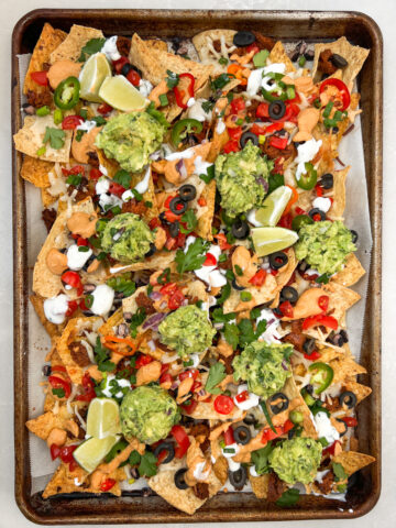 Baking sheet with vegan nachos topped with guacamole.