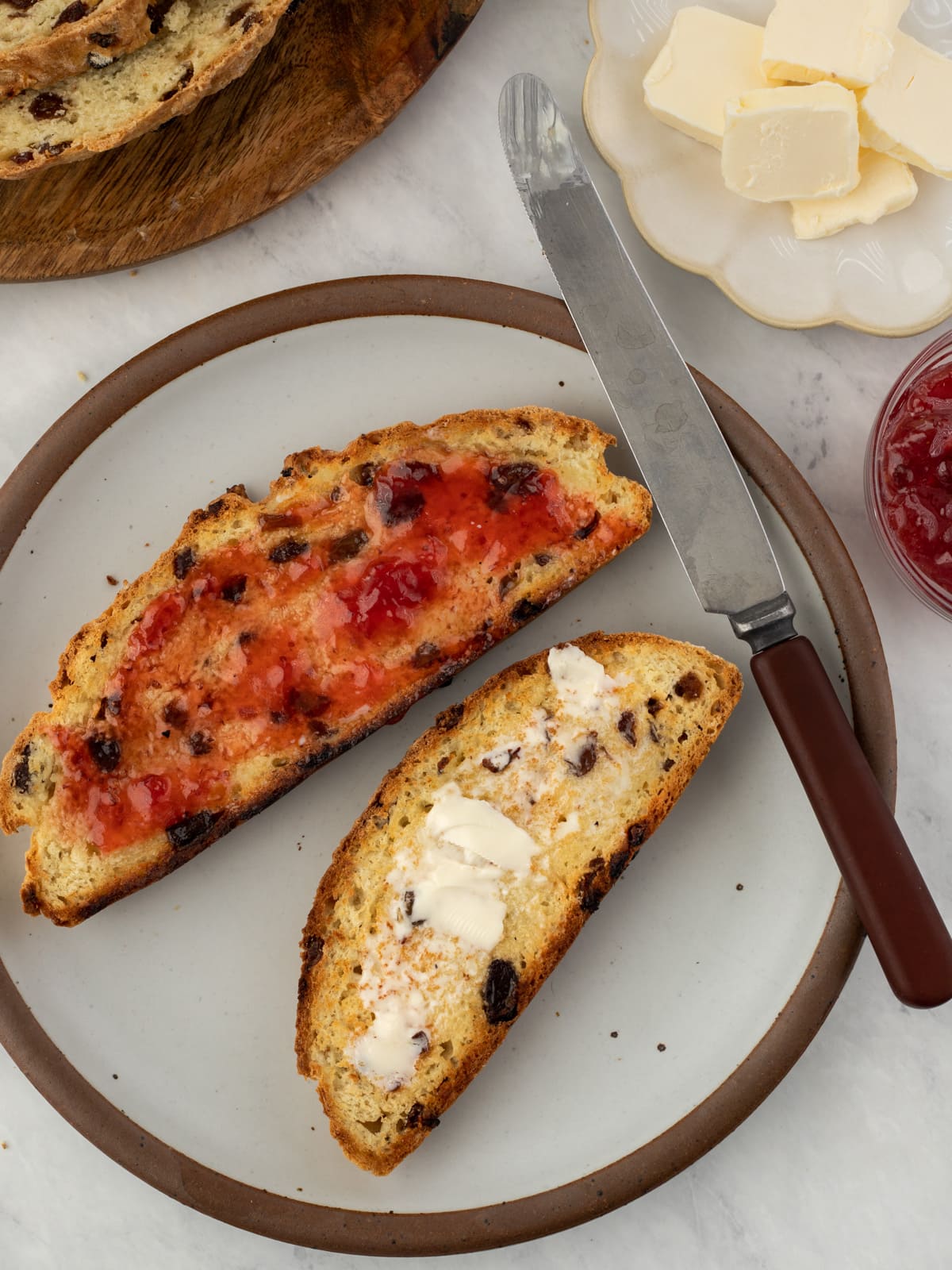 Two slices of soda bread slathered in butter and strawberry jam on a plate.