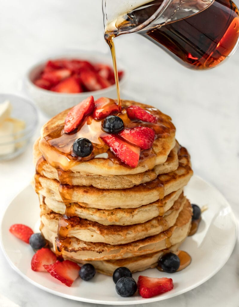 Stack of pancakes topped with berries with drizzled with syrup.