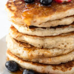 Stack of buttermilk pancakes topped with blueberries and strawberries.