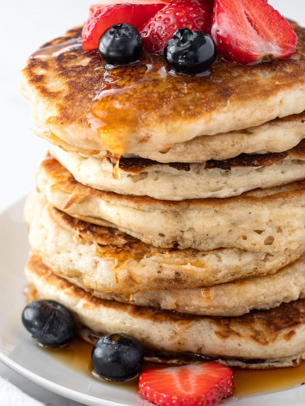 Stack of buttermilk pancakes topped with blueberries and strawberries.