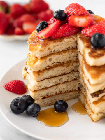 Stack of fluffy pancakes topped with fresh strawberries and blueberries.