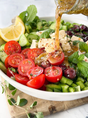 Greek salad dressing being poured over salad with olives and feta cheese.