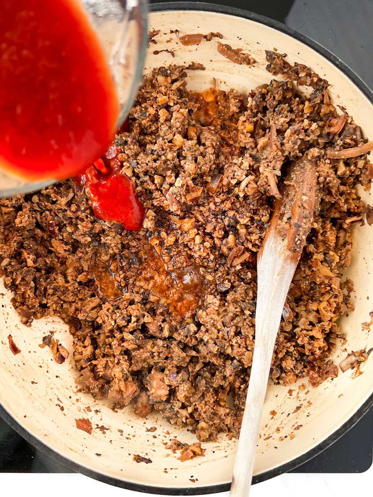 Tomato sauce being poured into ground walnut mushroom meat.