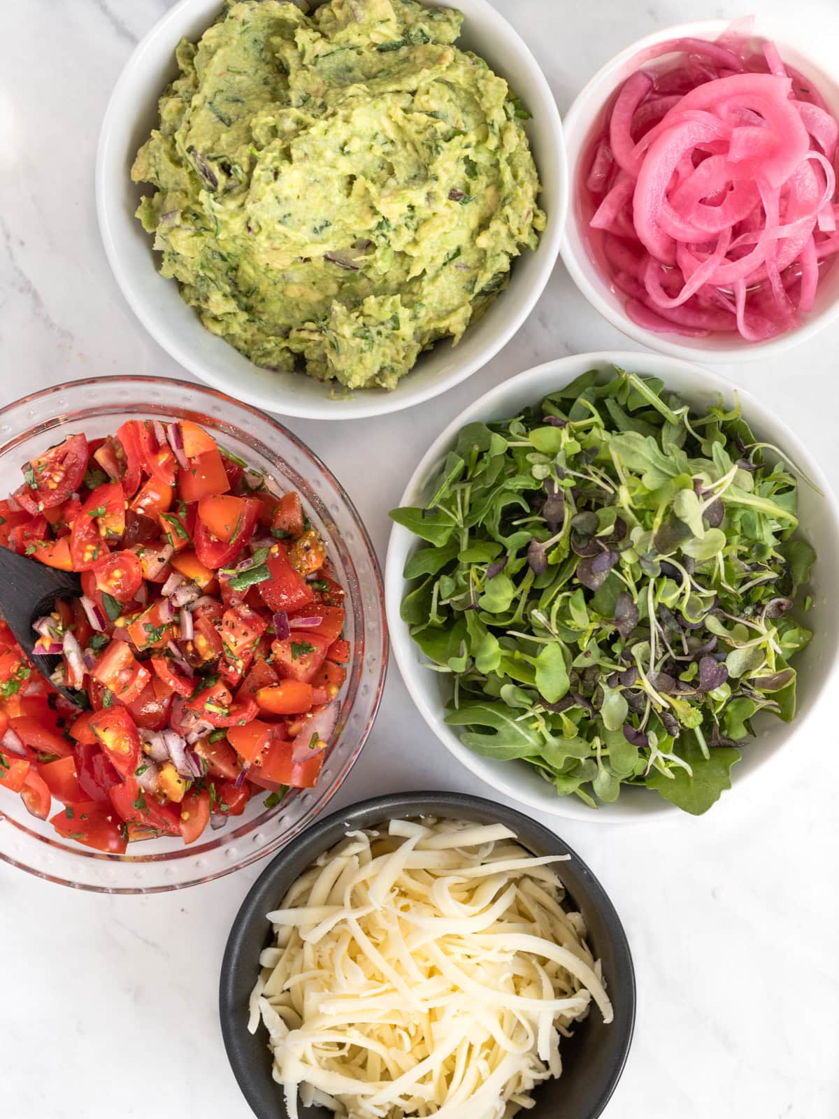 Taco toppings including guacamole, pickled onions, microgreens, pico and vegan cheese.