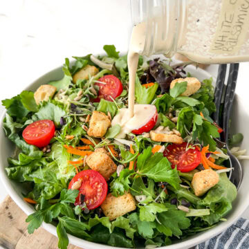 Creamy white balsamic dressing being poured onto a vibrant leafy green salad with tomatoes.