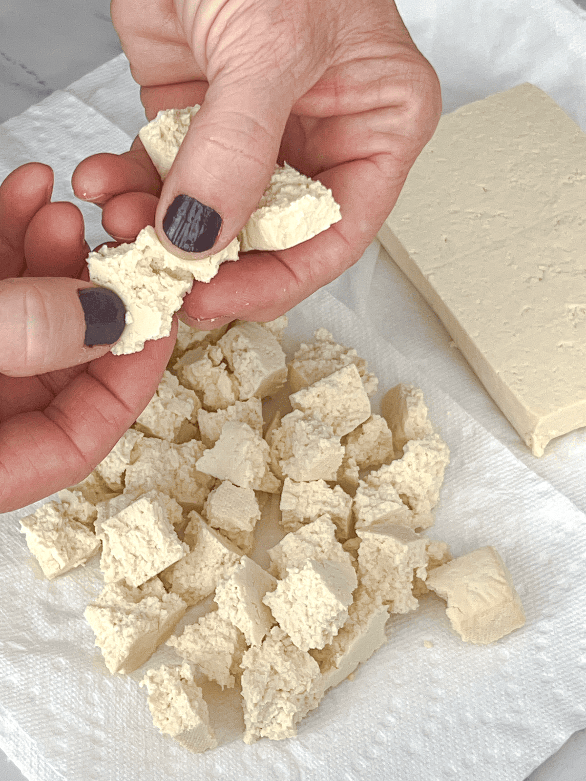 Block of extra firm tofu being broken into sausage size crumbles.