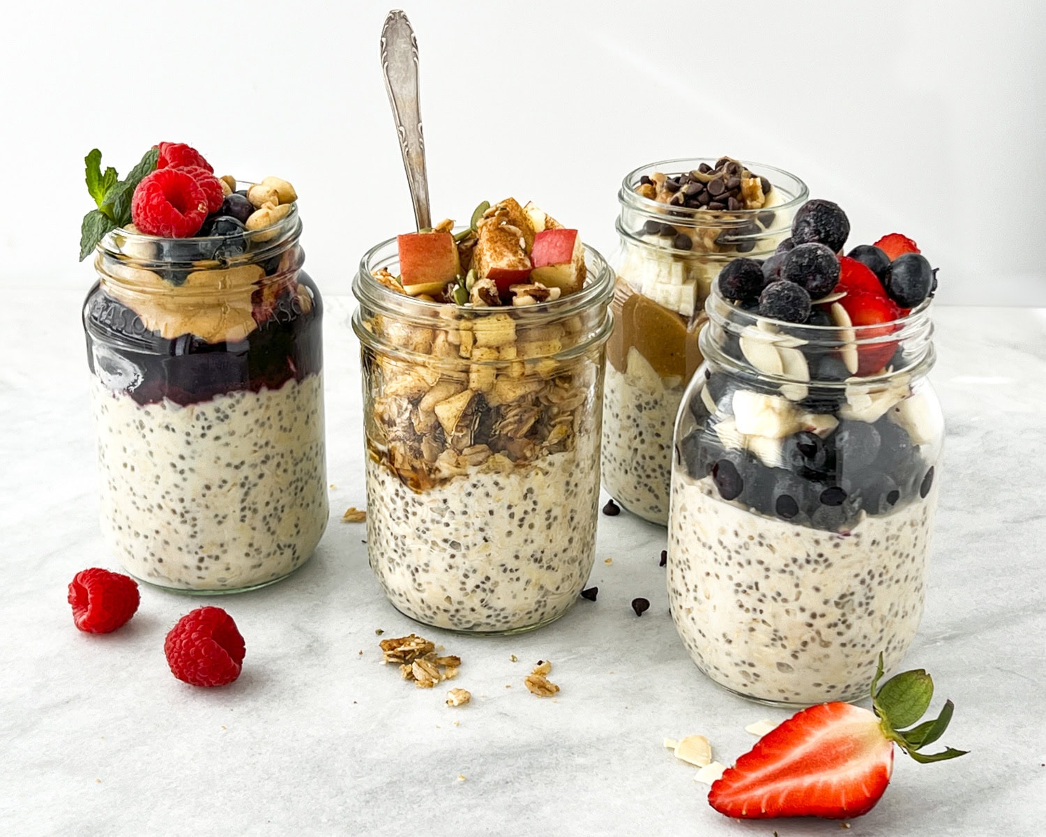 Four jars of overnight oats with various fresh fruit toppings.