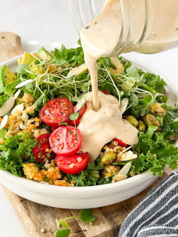 Creamy tahini dressing being poured onto a kale crunch salad.
